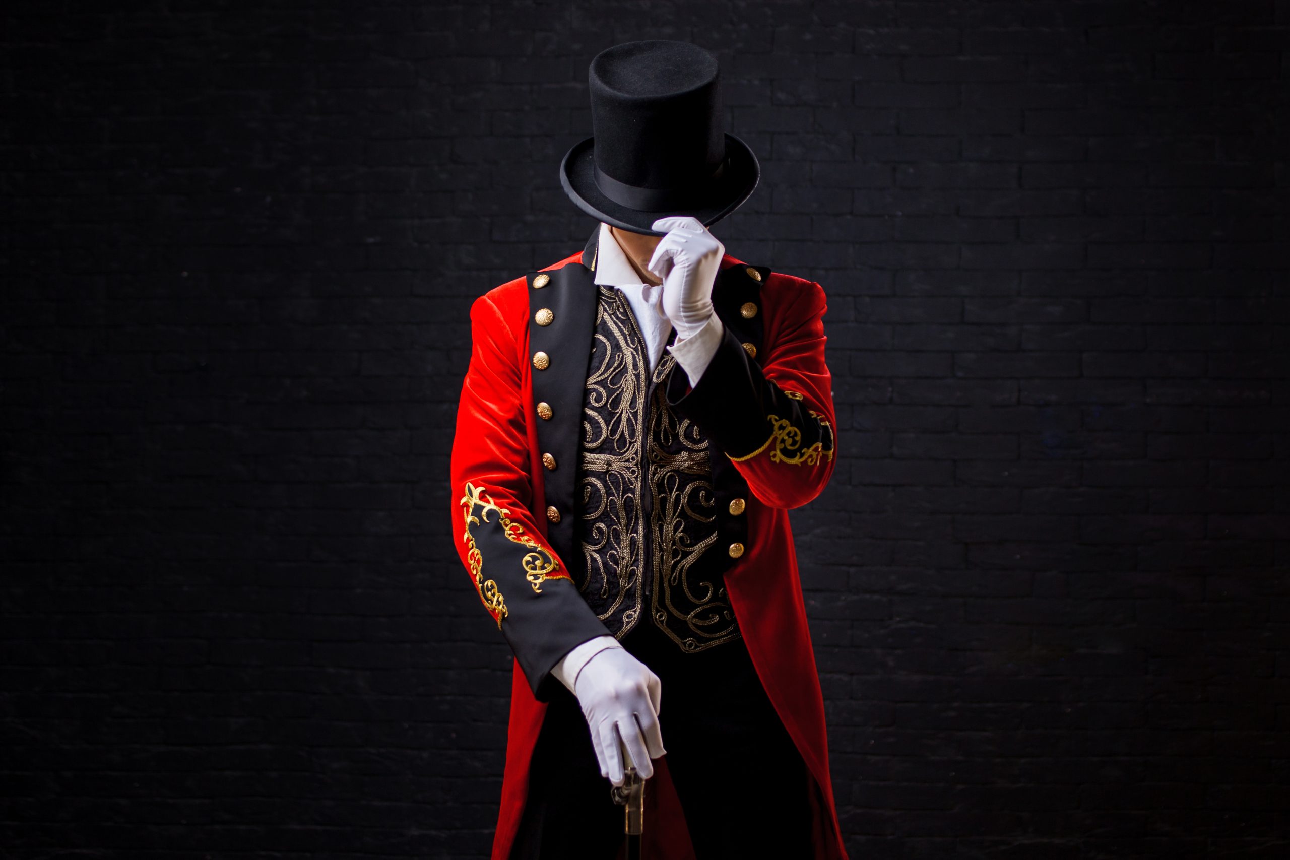 Showman. Young male entertainer, presenter or actor on stage. The guy in the red camisole and the cylinder. Looking down, hand on the hat